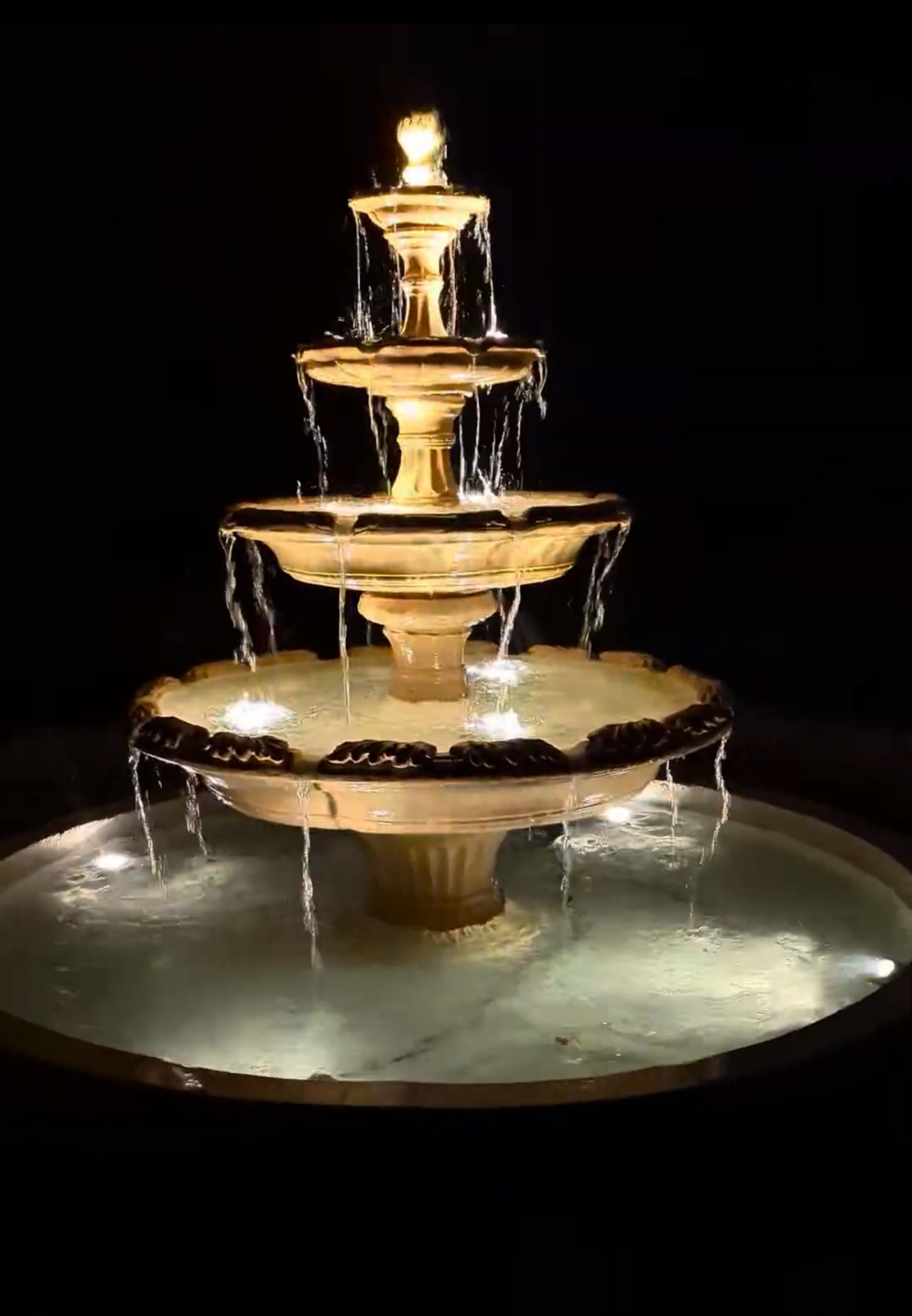 Tiered fountain lit at night. Water cascades down levels.