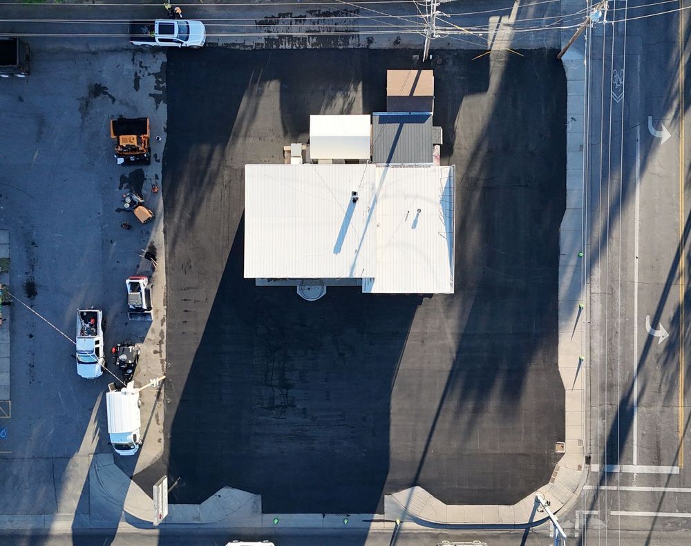 Aerial view of a newly paved lot with a building, vehicles, and shadows from the morning sun.