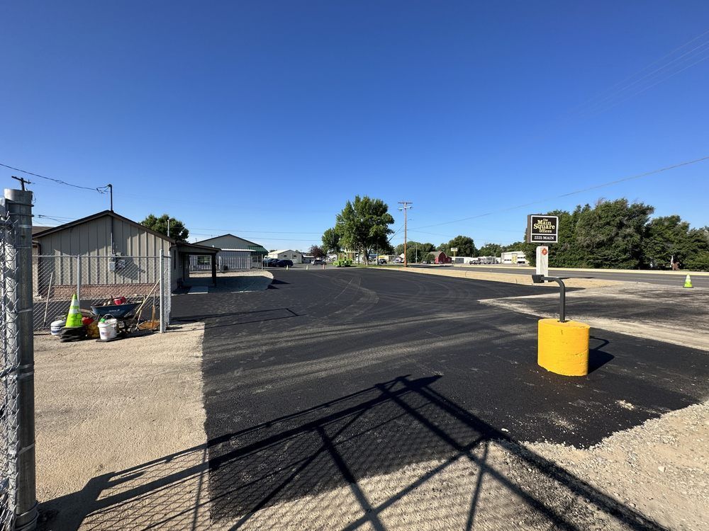 Newly paved parking lot under a bright blue sky. A few buildings are visible in the distance.