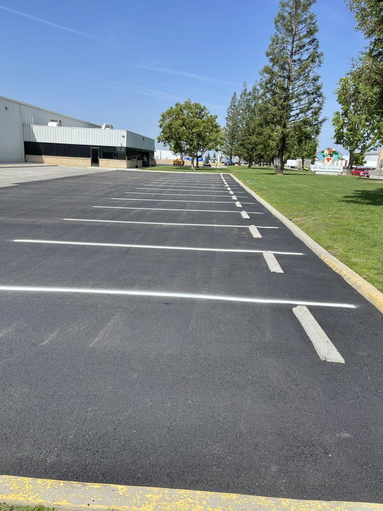 Empty asphalt parking lot with white painted lines, next to a grassy area, and a building.