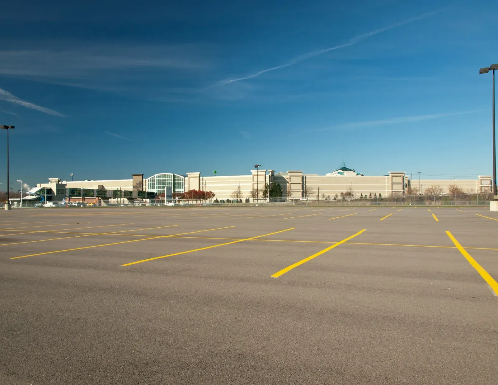 Empty parking lot in front of a large shopping mall under a blue sky.