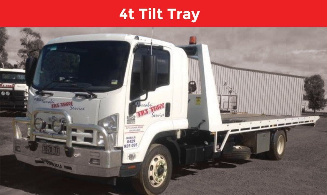 A 4t tilt tray tow truck is parked in front of a building