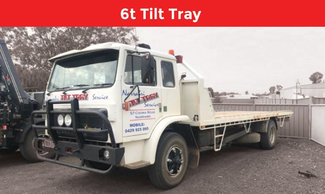 A white tow truck with a flat bed is parked in a gravel lot.