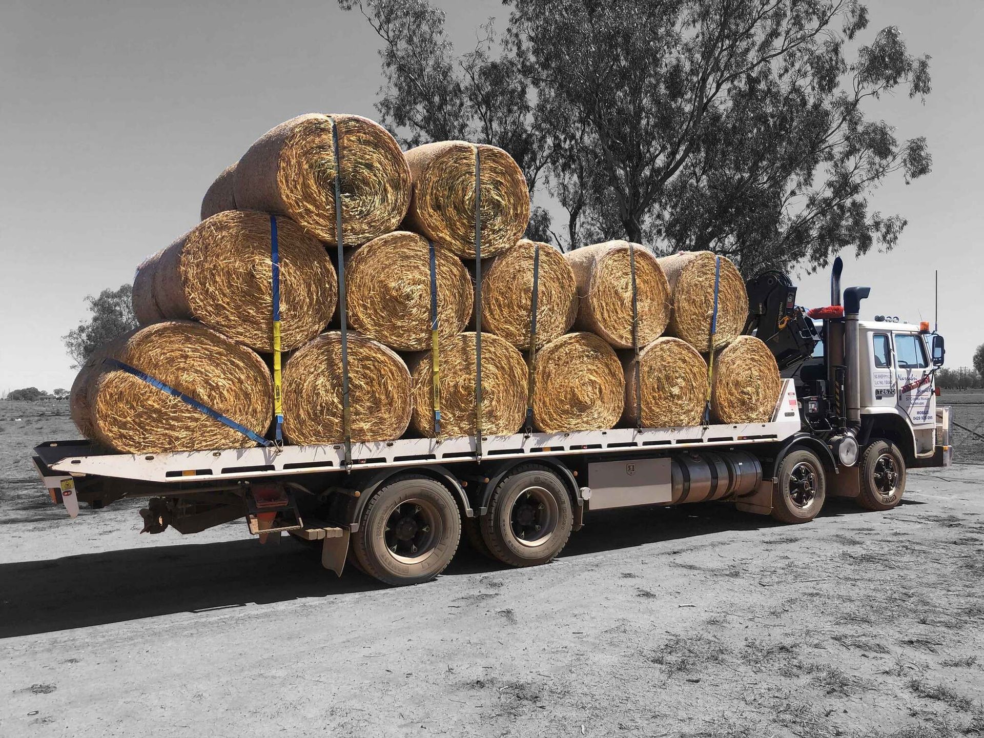 A truck is carrying a large stack of hay bales