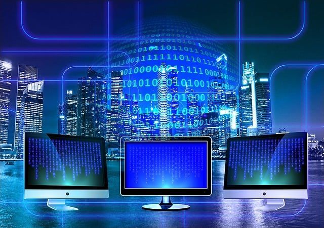 Three computers in front of a cityscape, overlaid with binary code and glowing blue lines.