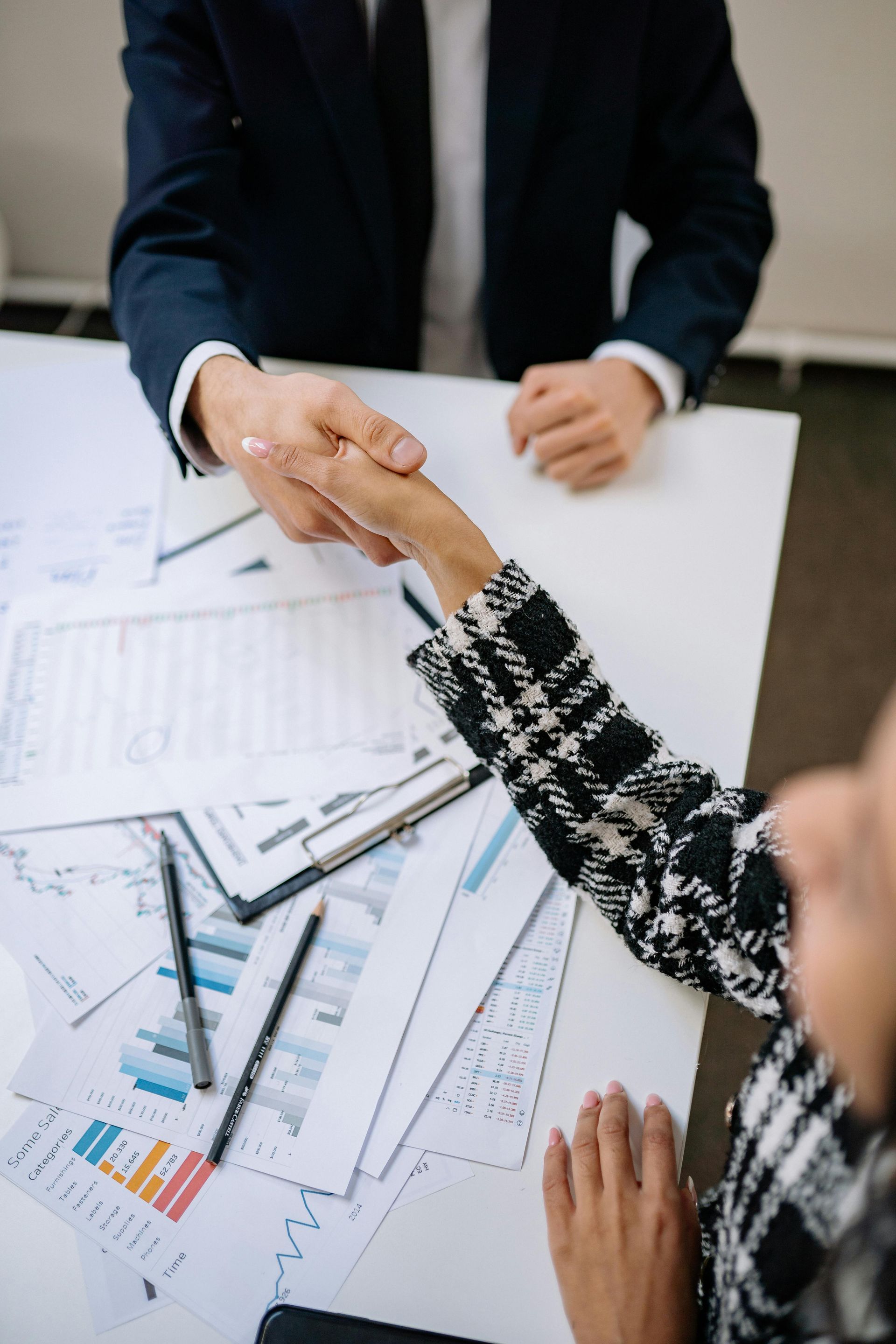 A man and a woman are shaking hands over a table.