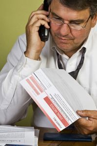 A man is talking on a cell phone while holding a mail notice