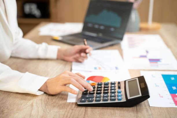 Local tax consultant analyzing charts and using a calculator at a wooden desk.