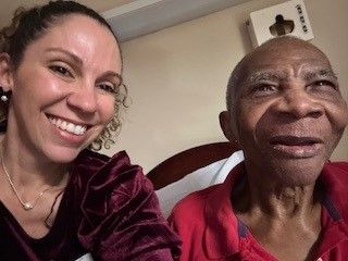 Two women are smiling for a picture while one of them is laying in a hospital bed.