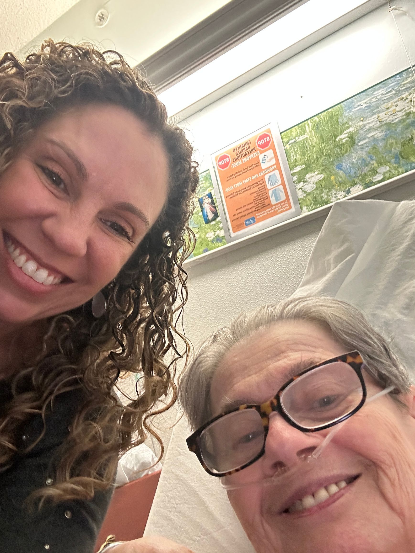 Two women are smiling for a picture while one of them is laying in a hospital bed.