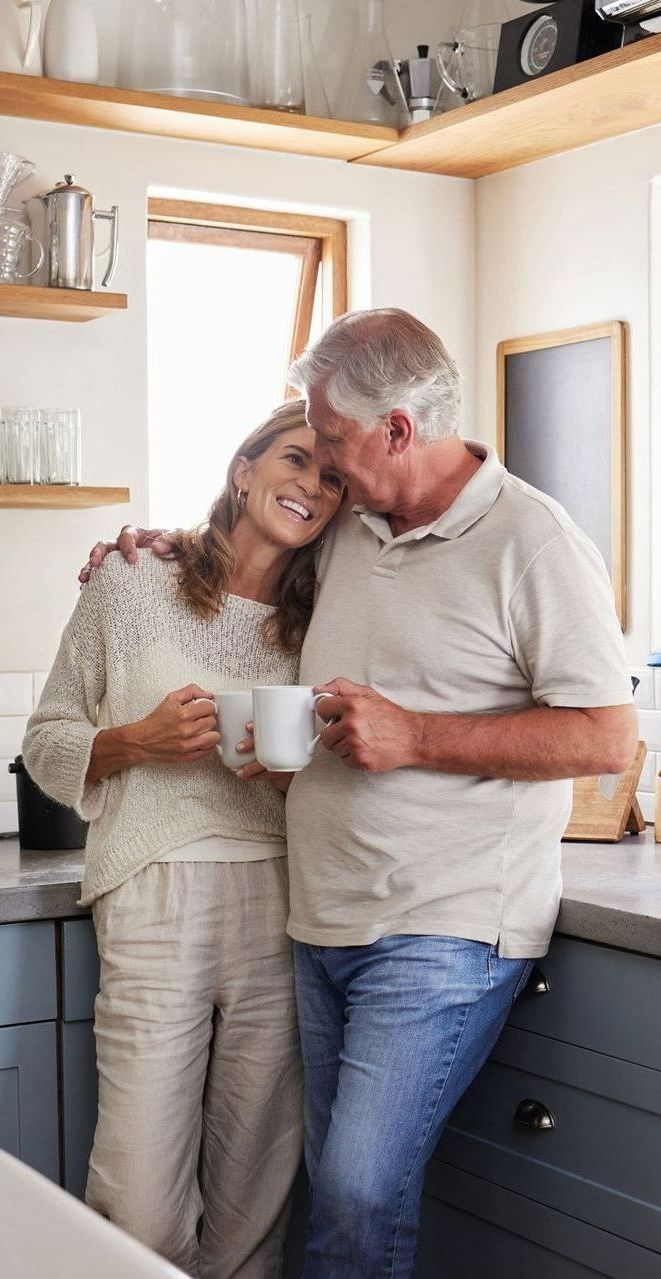 A man and a woman are standing in a kitchen holding cups of coffee.