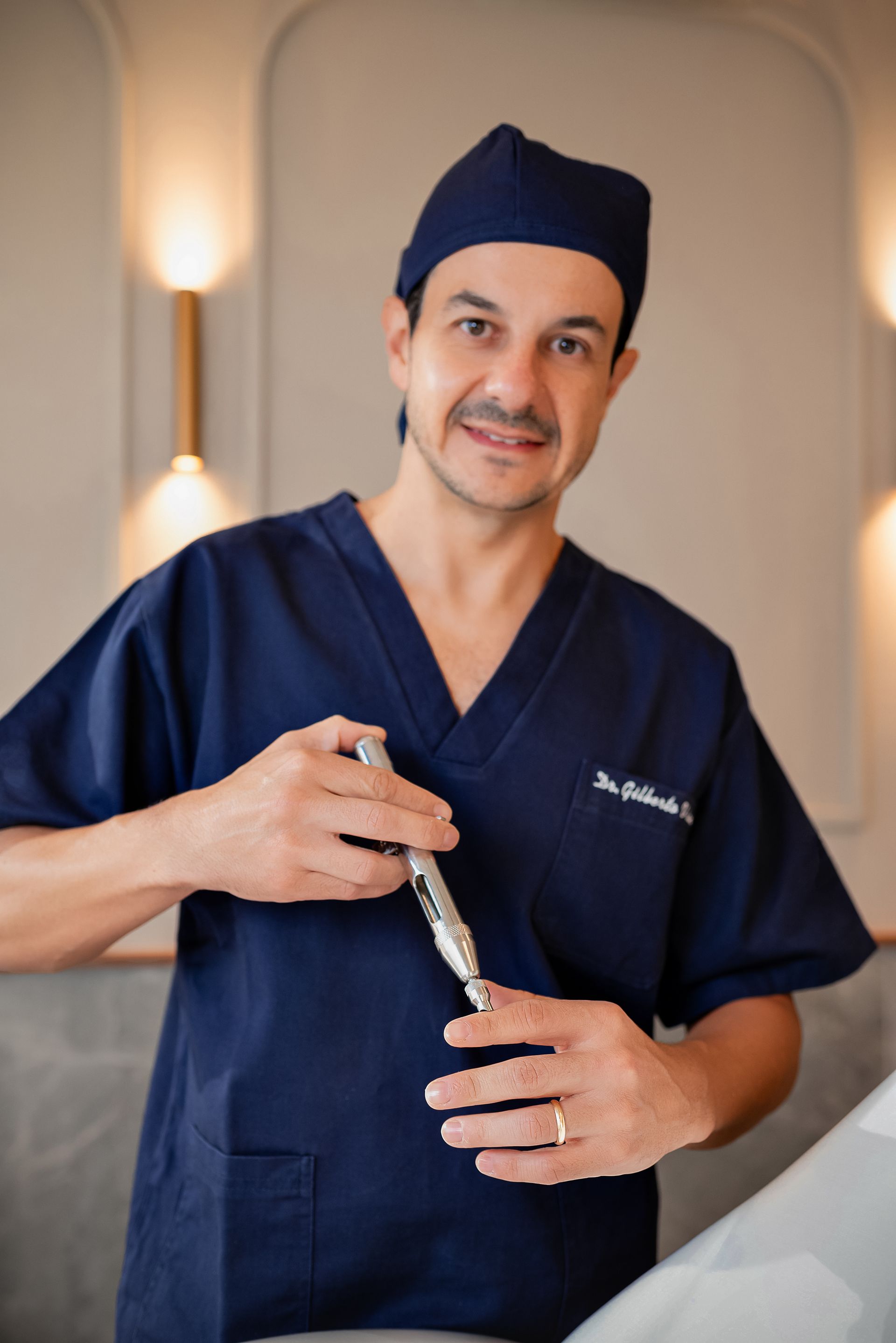 A man in a blue scrub top and hat is holding a pen.
