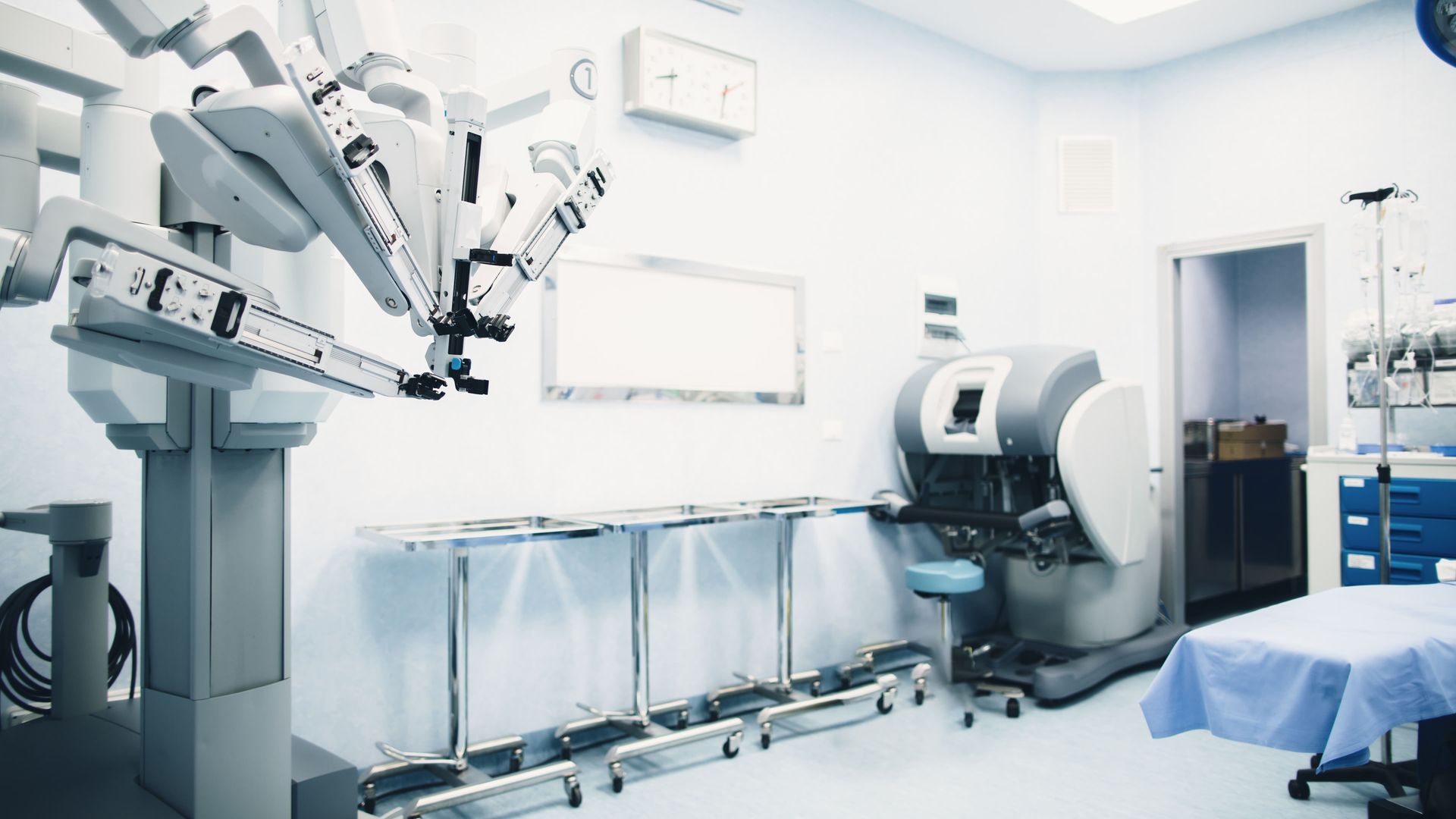 An empty operating room with a robotic arm and a table.
