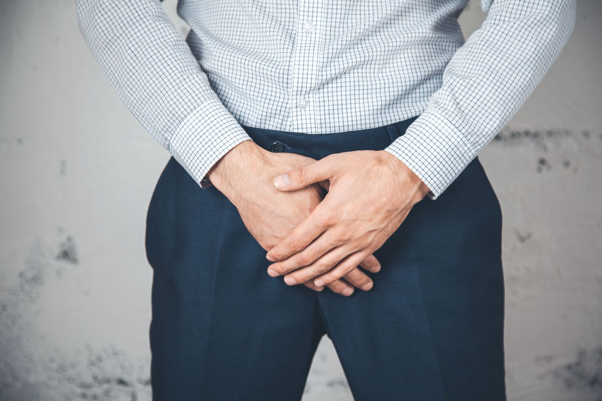 A man in a plaid shirt and blue pants is holding his hands over his stomach.