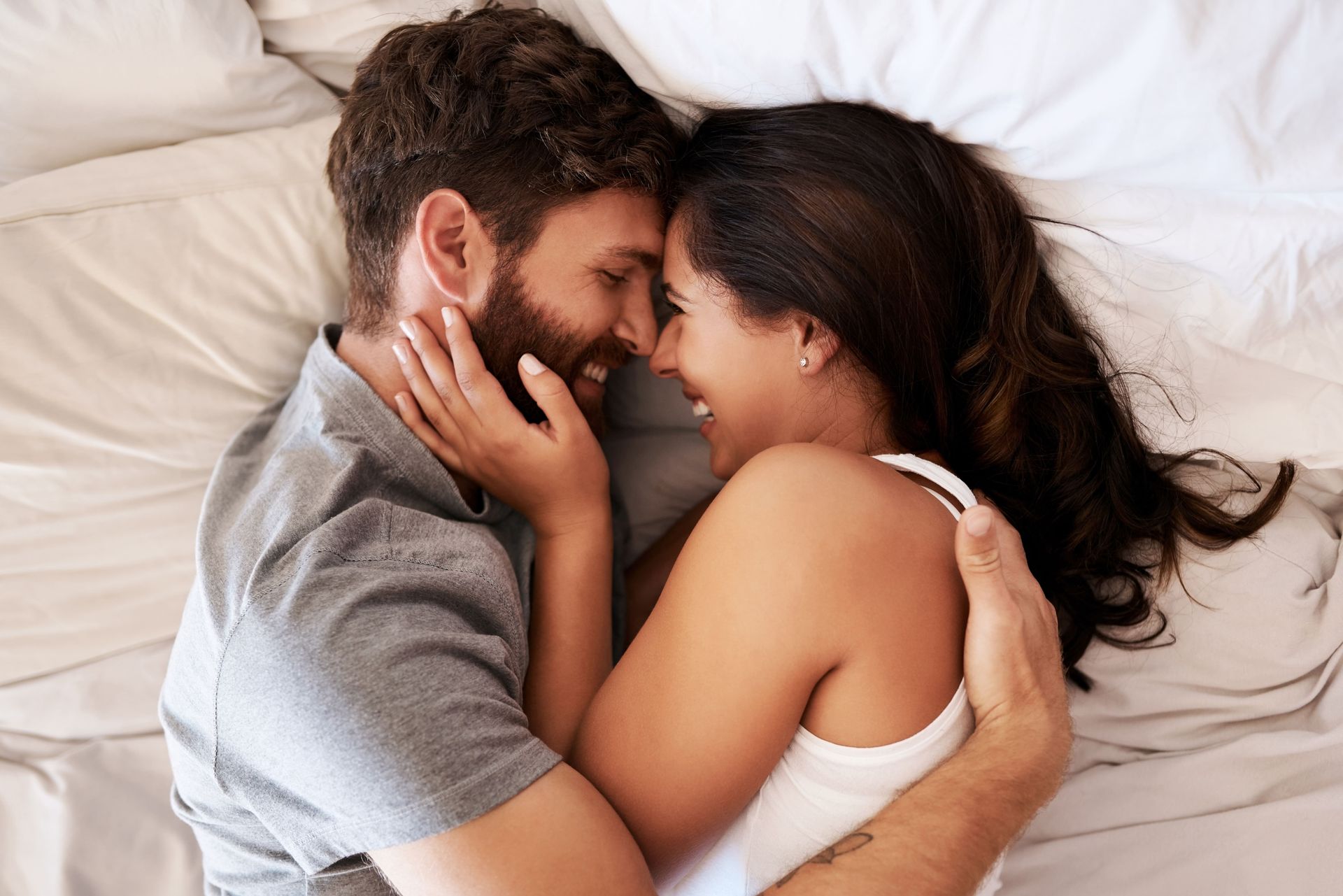 A man and a woman are laying on a bed hugging each other.
