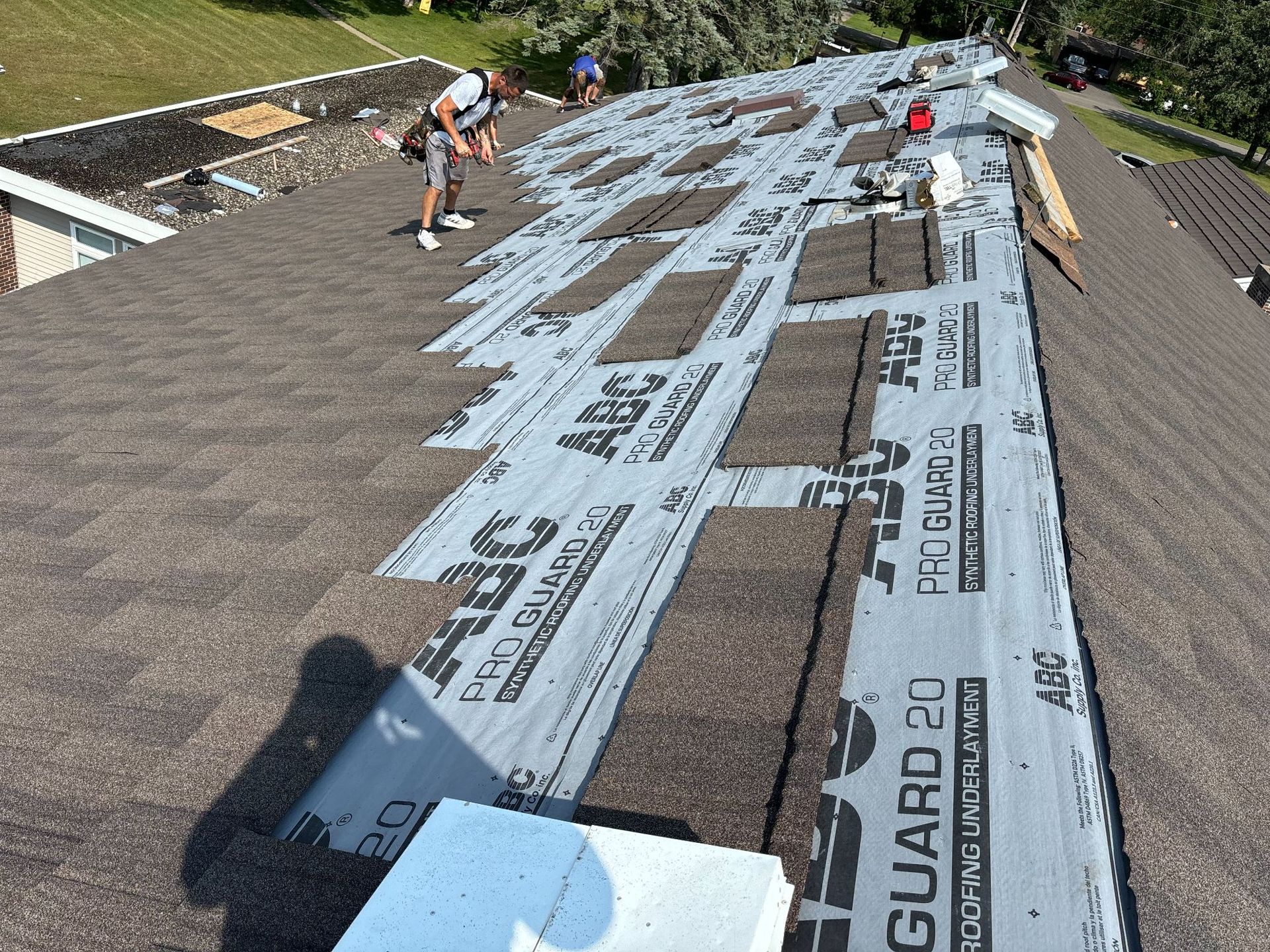 A man is standing on top of a roof covered in a roofing material.