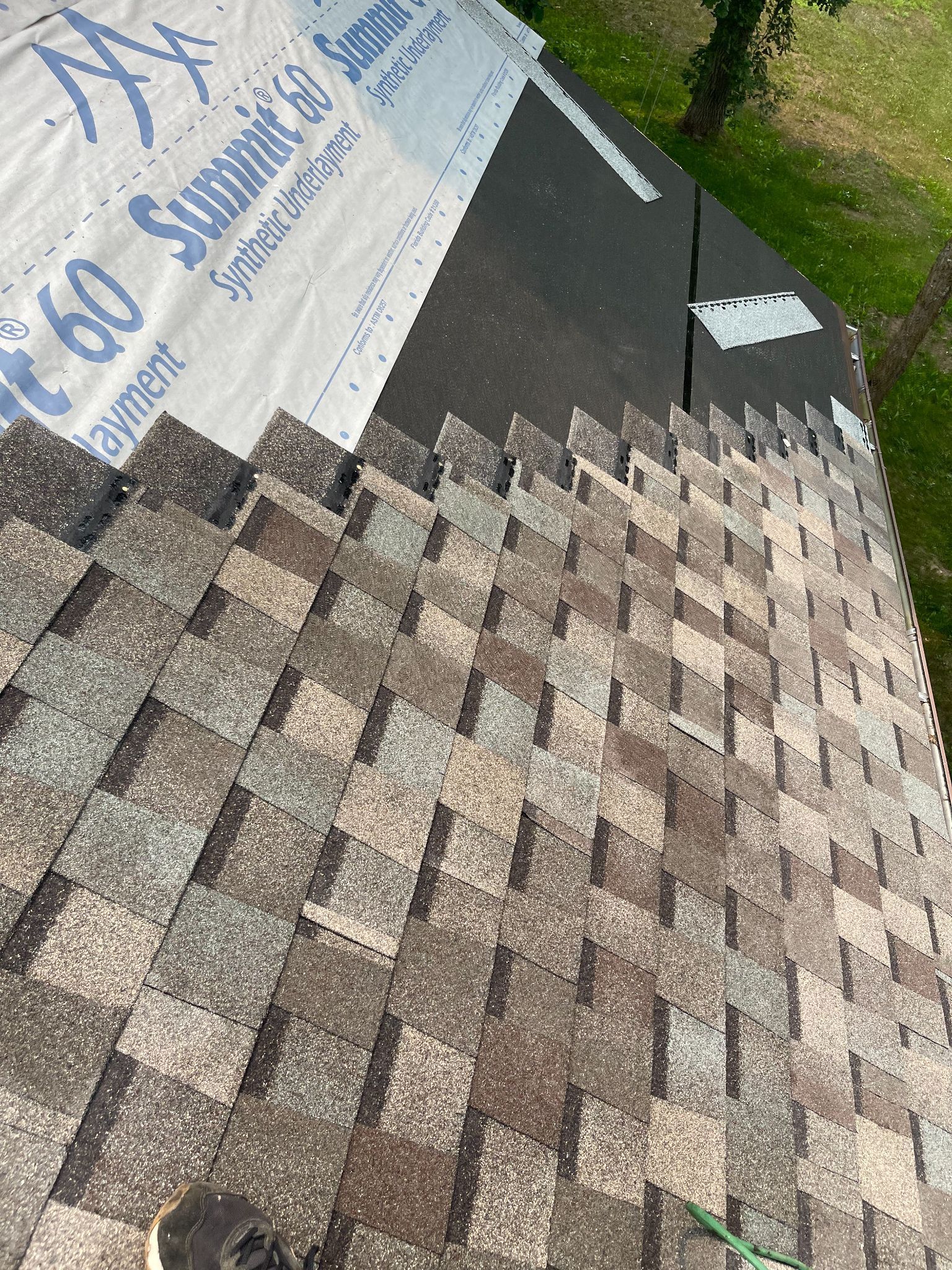 A person is standing on top of a roof with shingles on it.