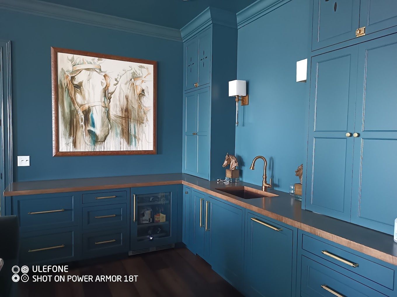 A kitchen with blue cabinets , a sink , and a painting on the wall.