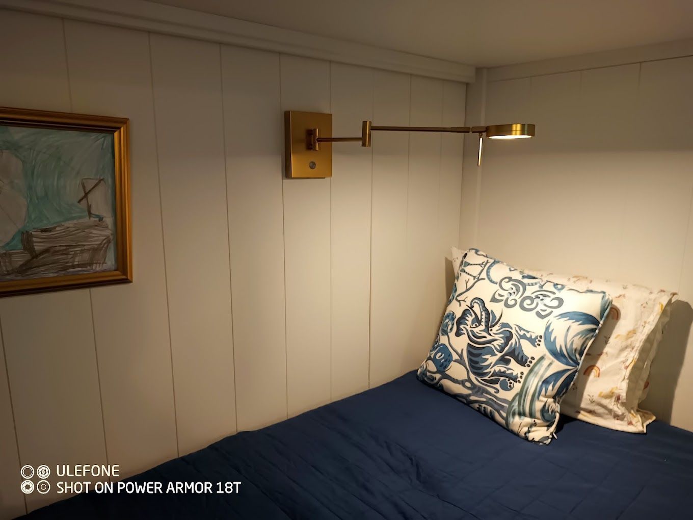 A bedroom with a bed , pillows , a lamp and a painting on the wall.