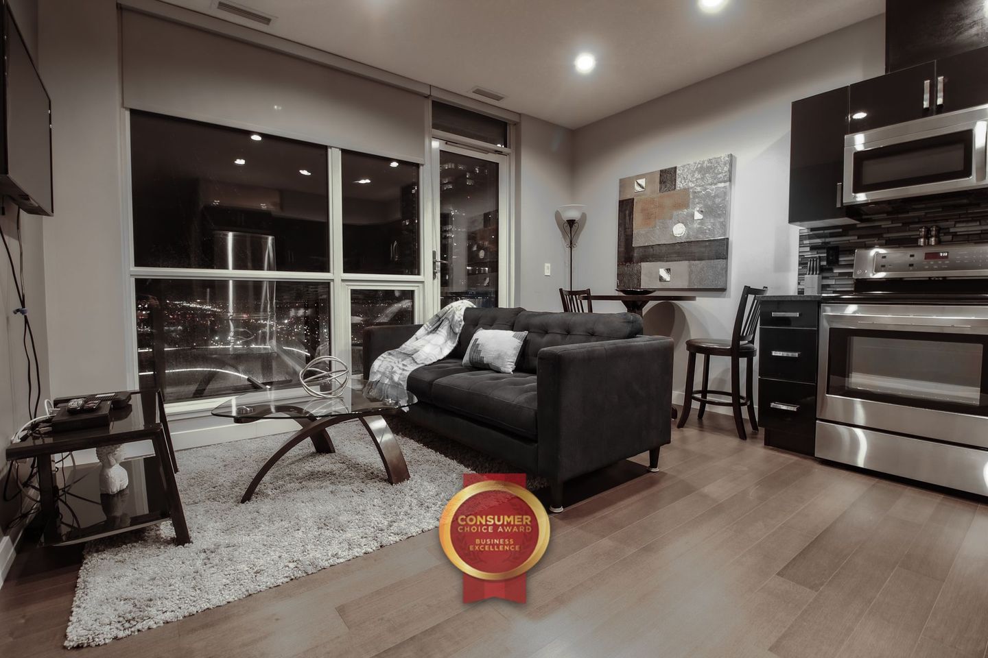 Large bedroom with grey bed and white linens on the bed daytime,  Dark espresso coloured hardwood flooring