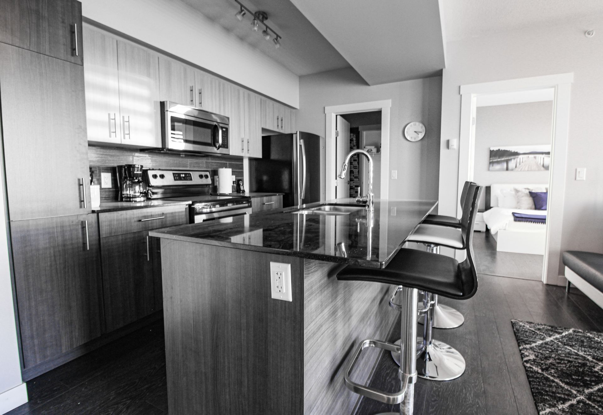 Modern kitchen with island and stools, doorway to bedroom in background.