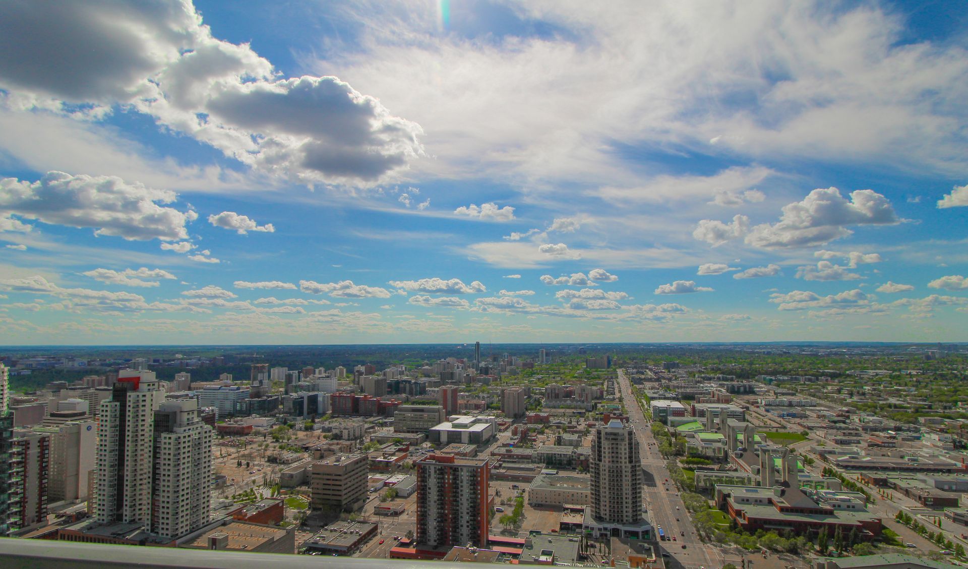 Cityscape under a blue sky with fluffy clouds. Buildings and streets stretch to the horizon.