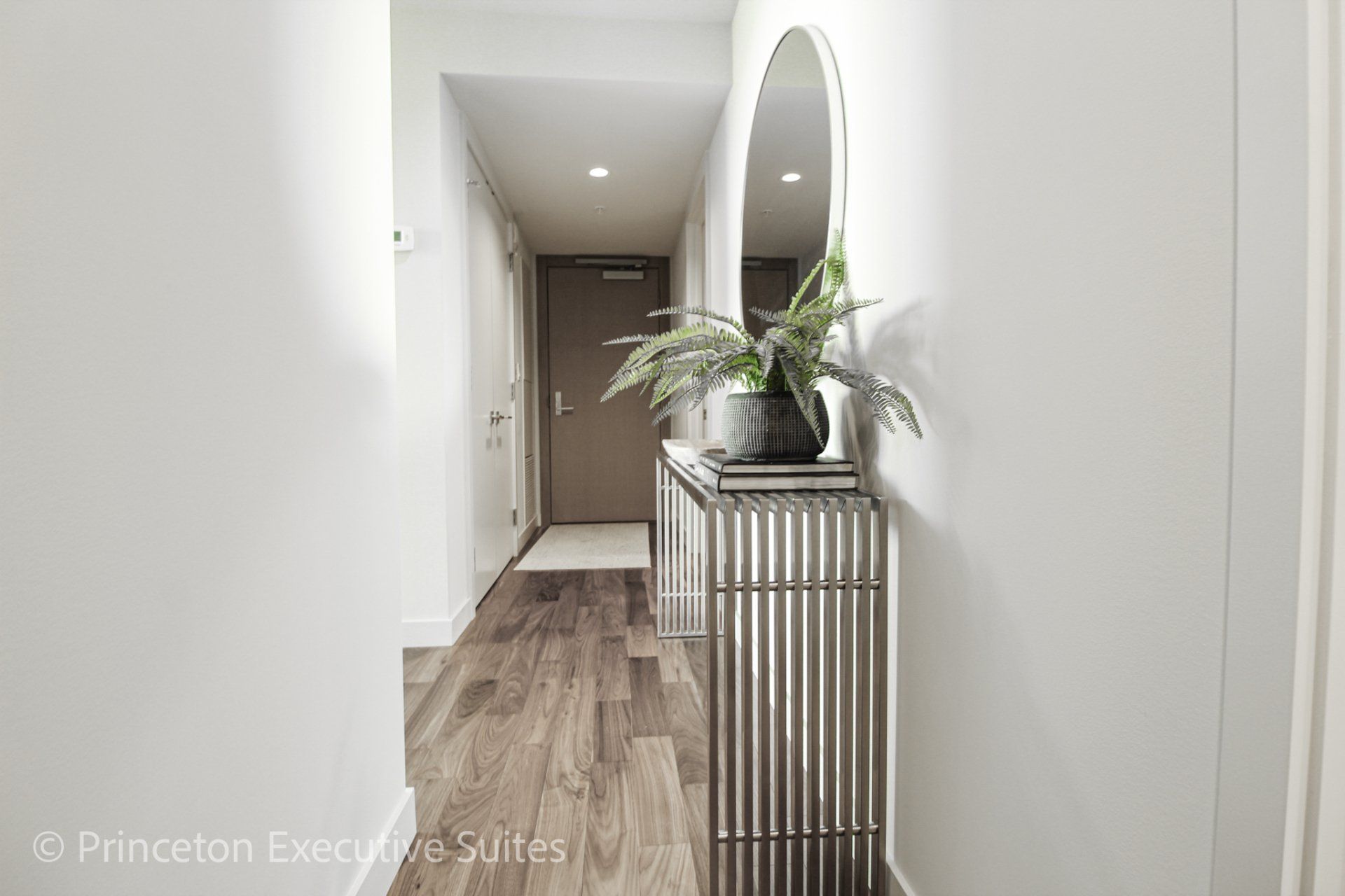 Front entrance hallway with a glass table with pewter coloured metal legs.  The front entrance door is in the background  of this edmonton furnished back ground in this edmonton furnished apartment