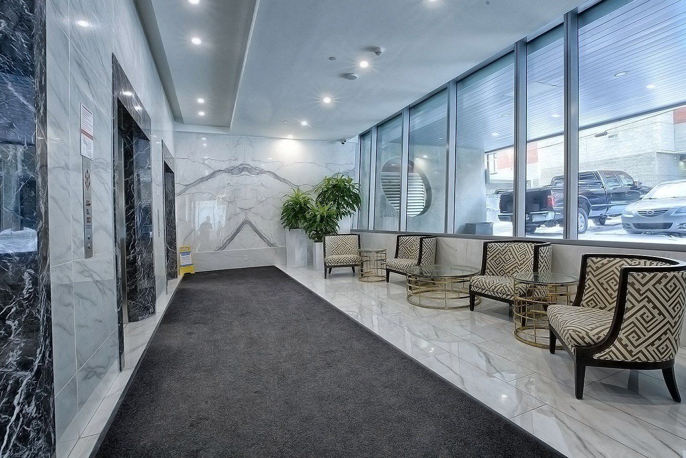 3 Stainless steel elevators with 6 elegant chairs in this seating area.  Modern white marble flooring and a large ceiling in to floor downs behind the seating area