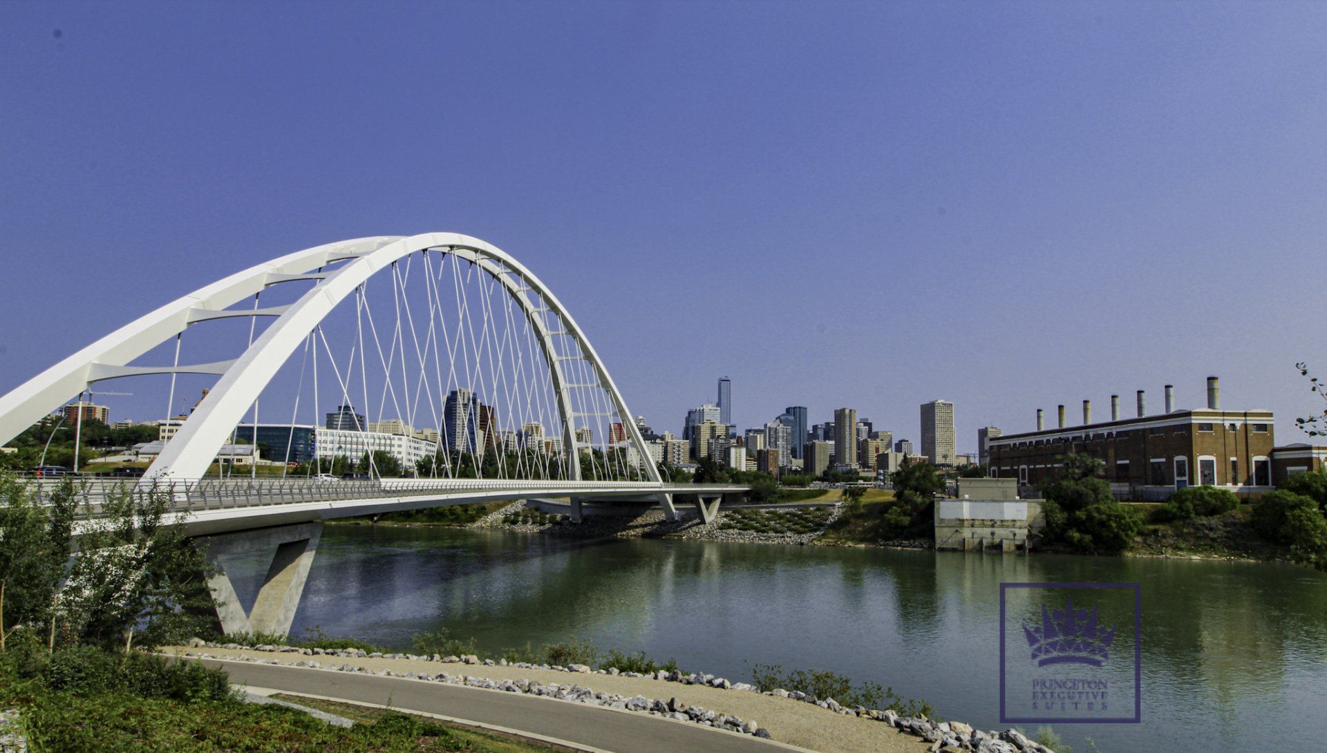 White arched bridge over a river, cityscape in the background, sunny day.