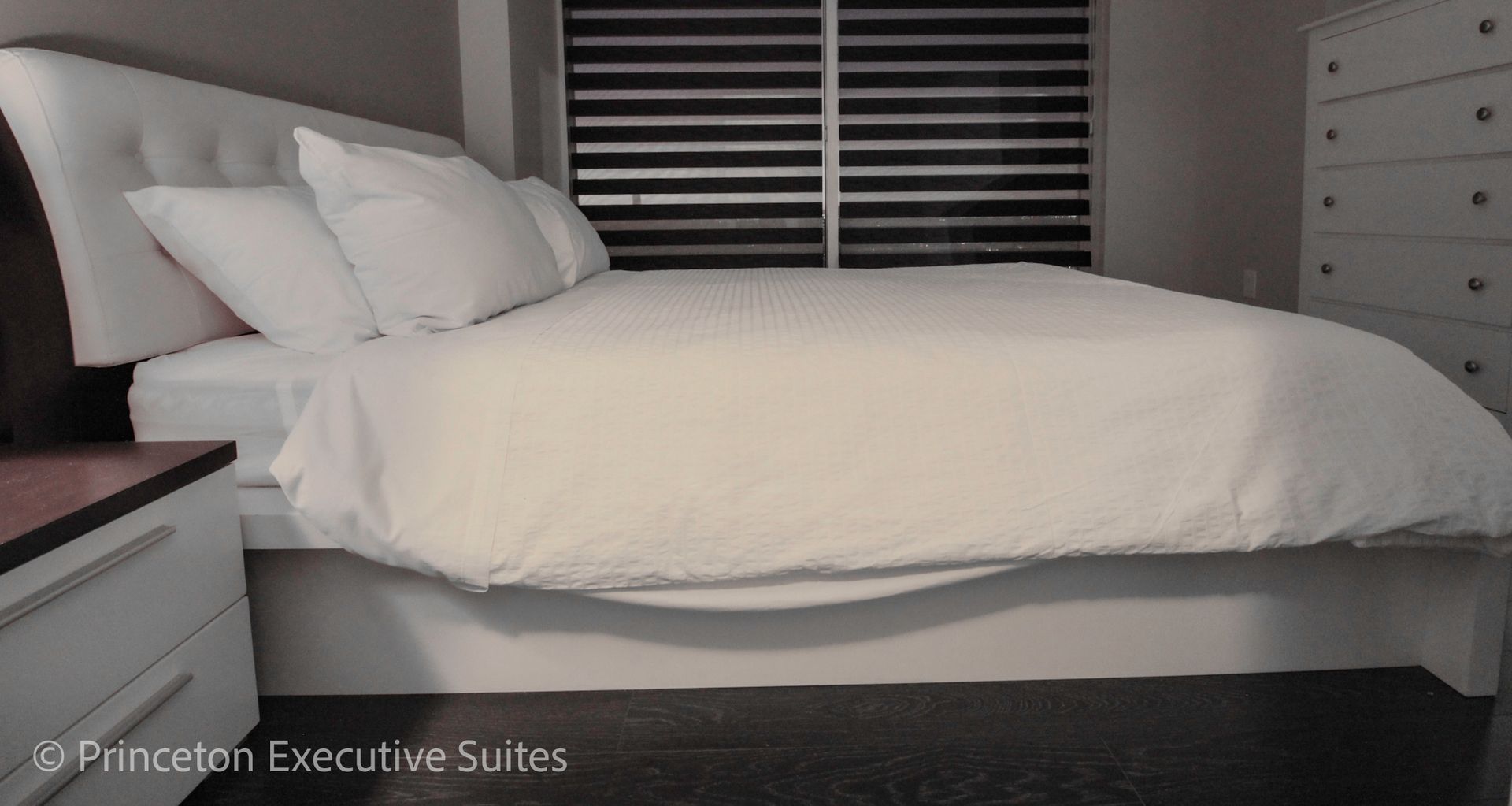 White bed in bedroom with matching headboard, pillows, and window blinds.