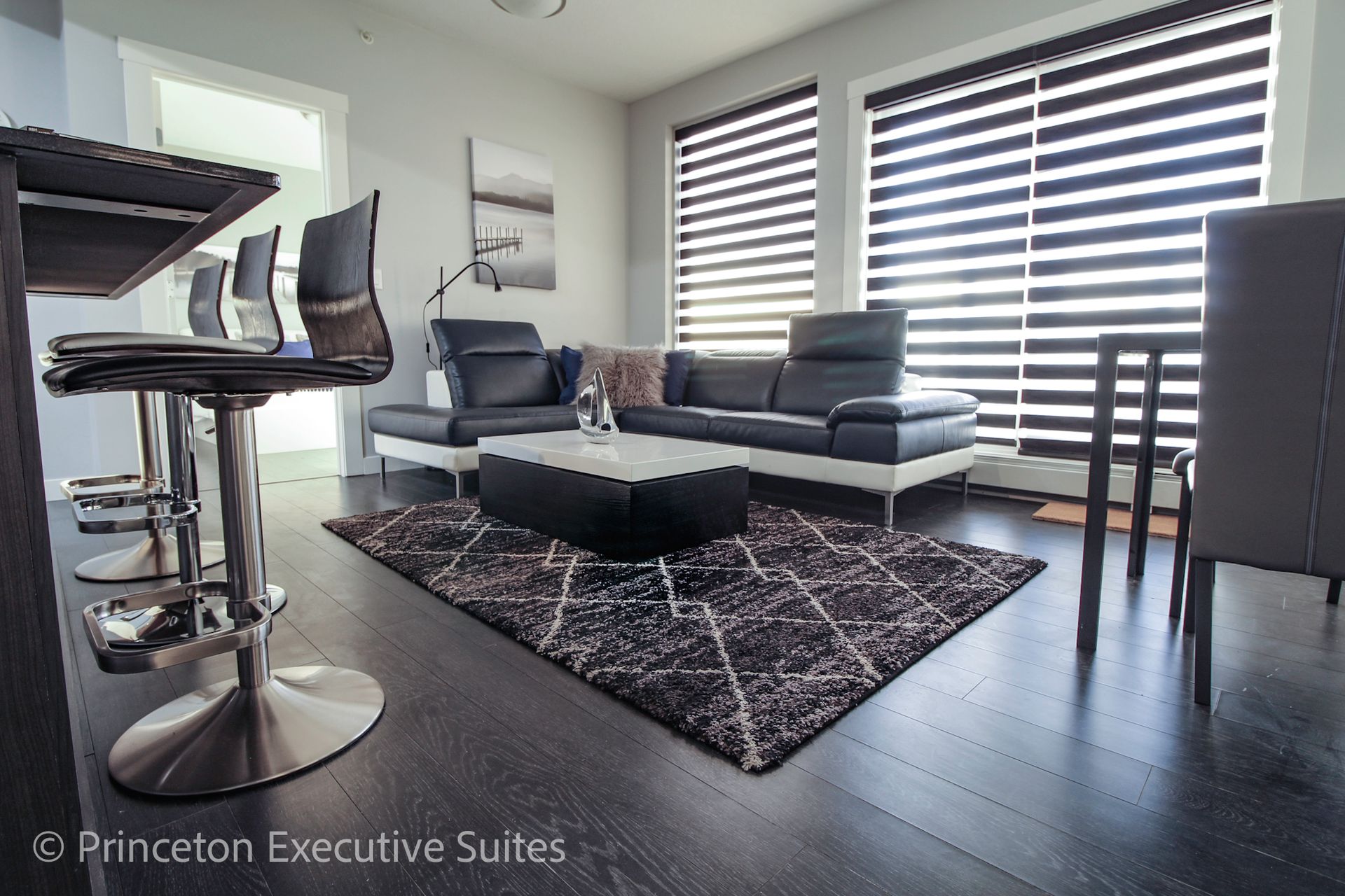 Modern living room with black and white decor, bar stools, and a rug.