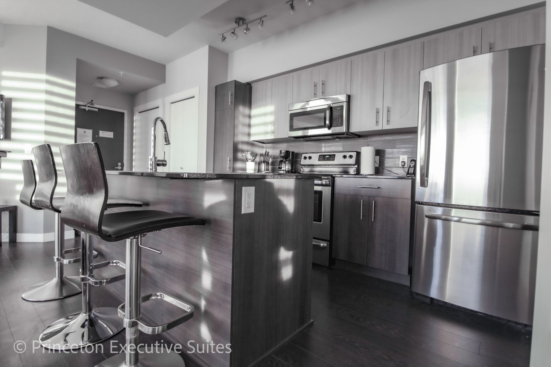 Modern kitchen with an island, stools, stainless steel appliances, and wooden cabinets.