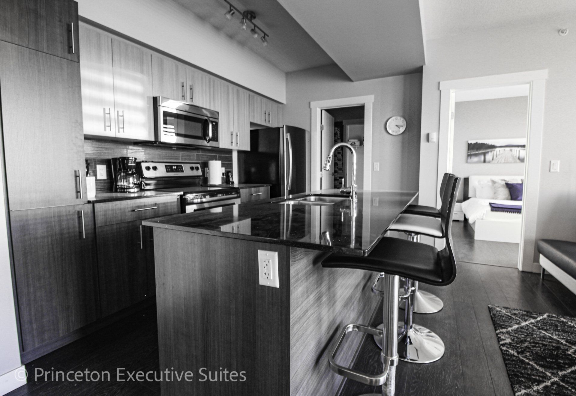 A immaculate kitchen with Grey cabinets black granite counter tops, stainless steel appliances
