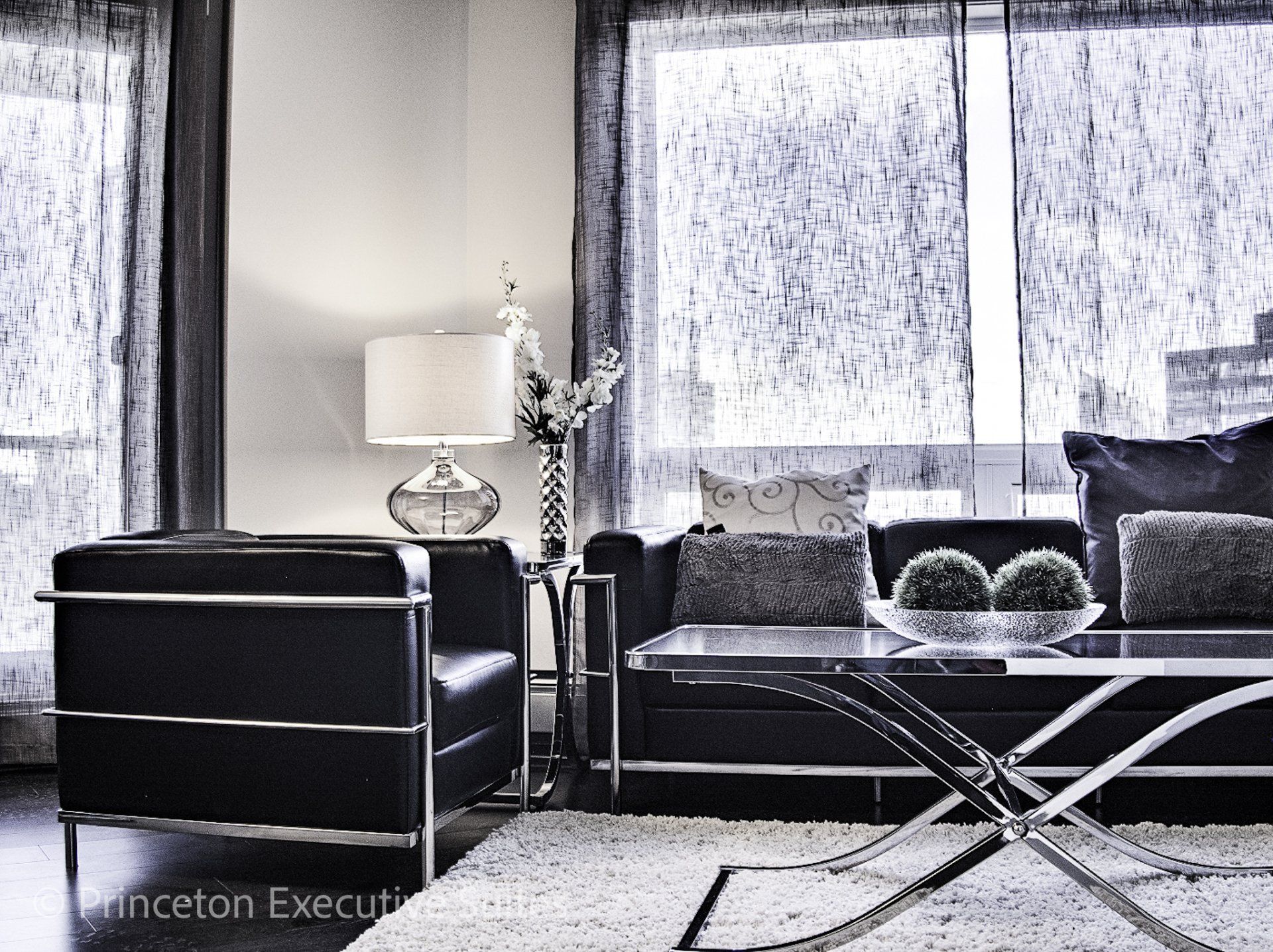 Modern Black couch, black chair and coffee table in front of a transparent curtained window Edmonton furnished executive apartments