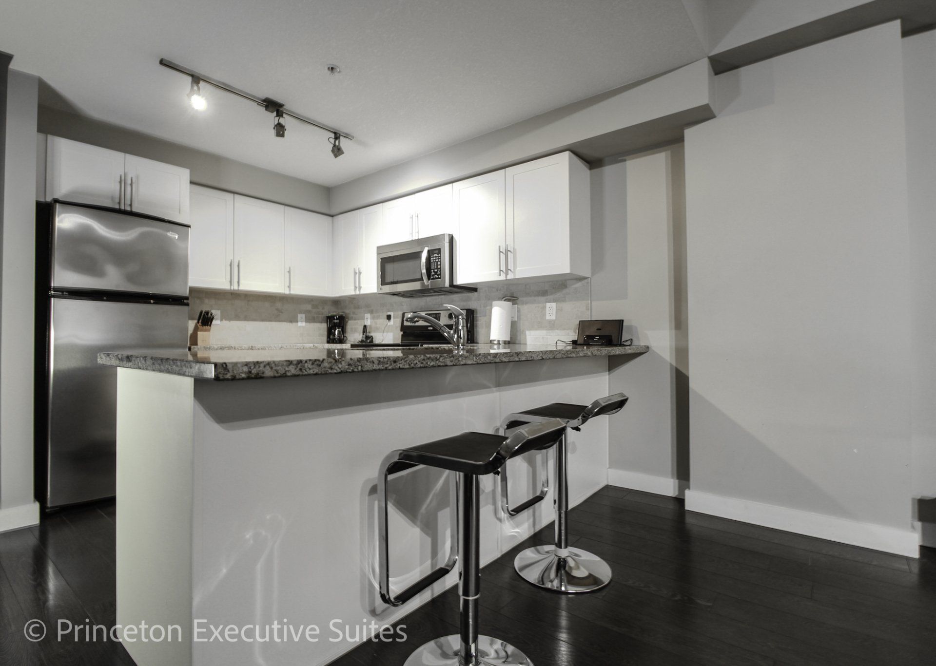 white kitchen and white kitchen with  black granite counter tops black metal barstools in front of eating bar in an Edmonton extended stay suite
