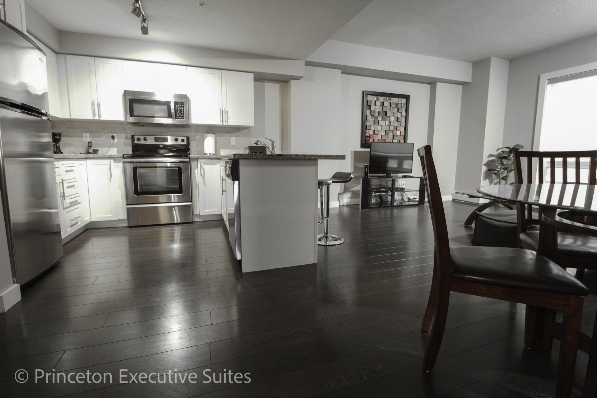 Dark hardwood flooring white contrasting kitchen cupboards and stainless steel appliances are a feature of this Edmonton furnished suite