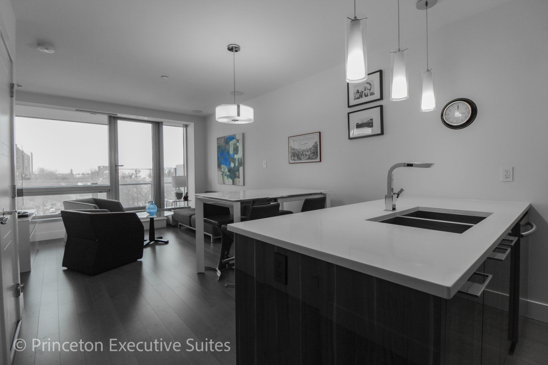 Edmonton executive suite with white quartz counter top  Modern fixtures and white glass dining table.   Ceiling to floor windows in front of a grey and black living room set