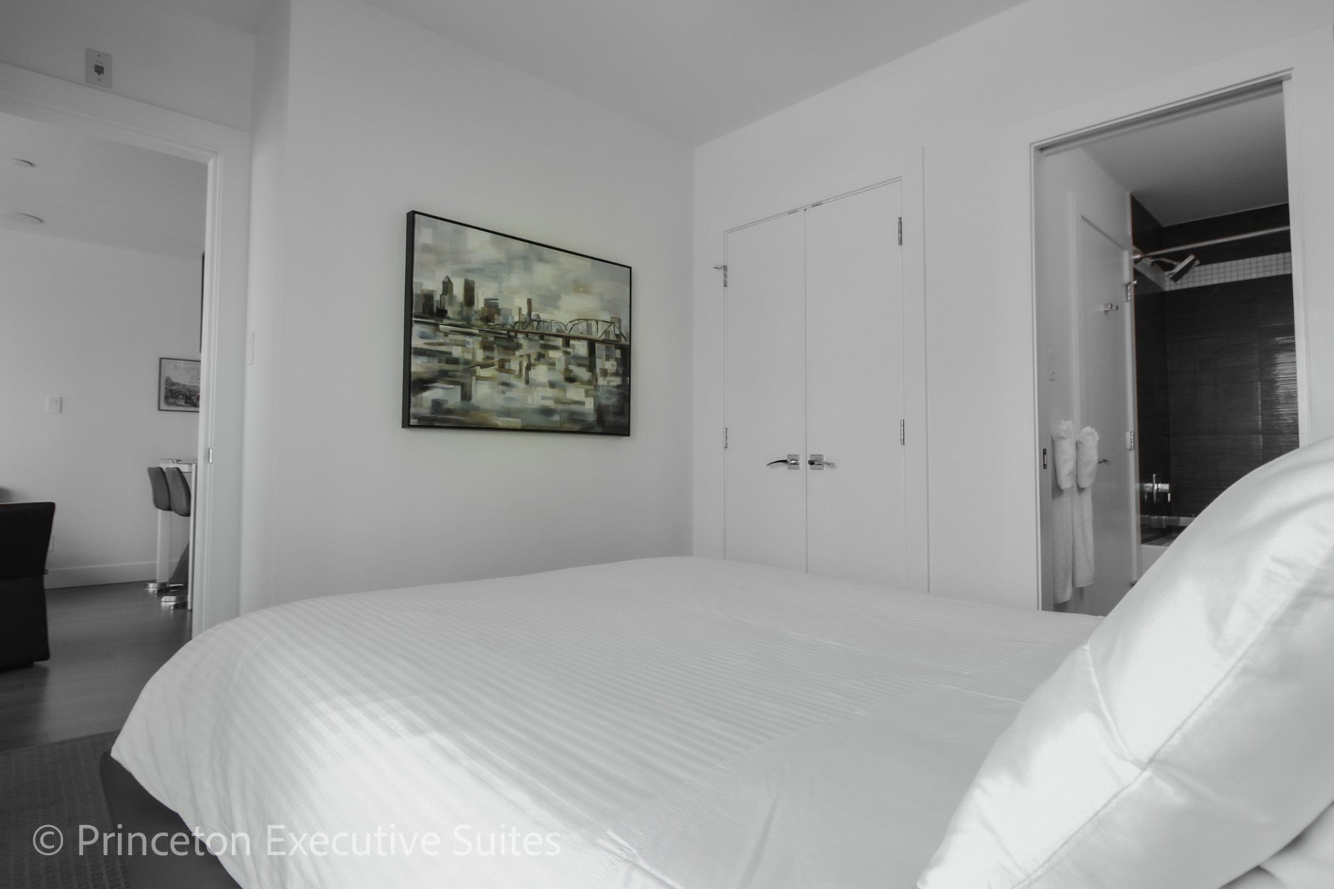 White foot of bed in this edmonton executive suite black and grey impressionist picture of a bridge in the back ground