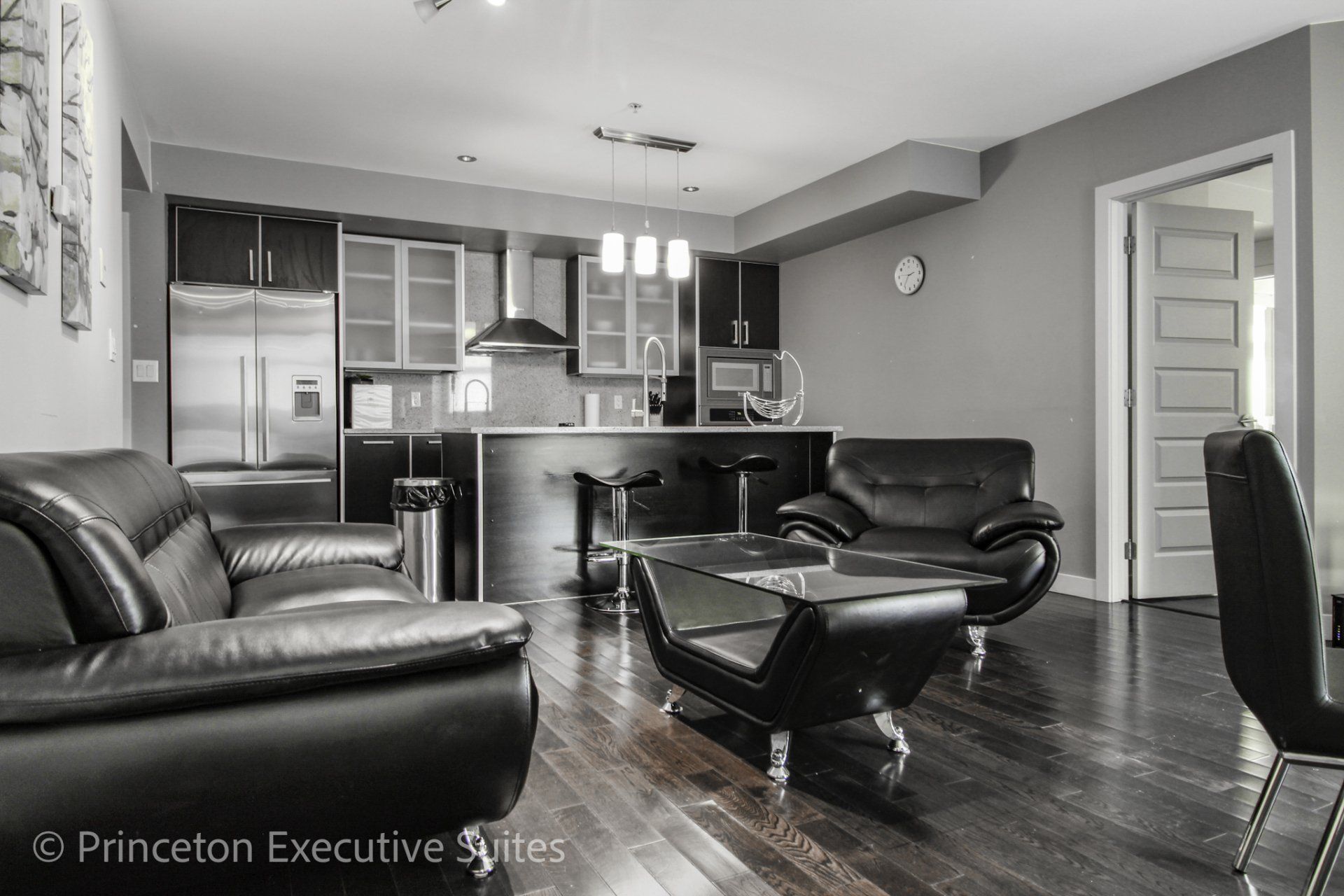 Black leather living room wiht espresso hardwood flooring stainless steel kitchen in back ground immaculate furnished suite in Edmonton