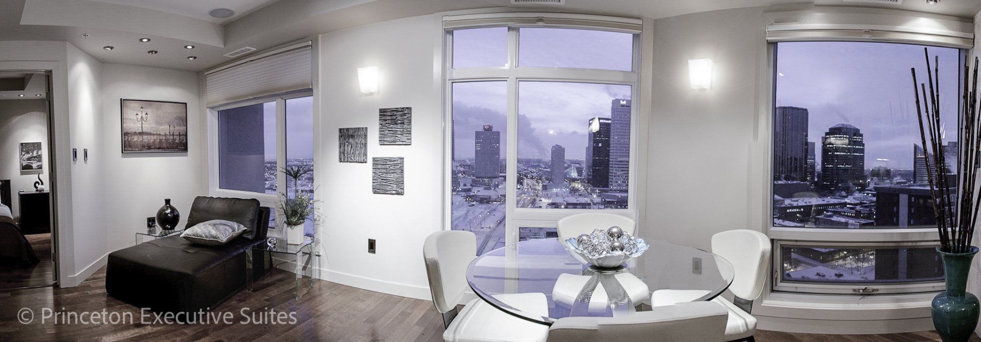 Wide shot of a edmonton luxury furnished suite with white leather dinette and chaise lounge beside ceiling to floor windows