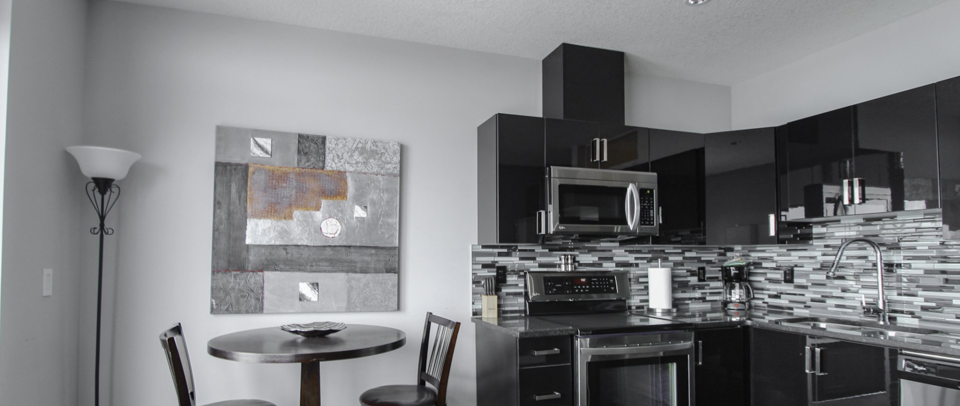 Kitchen area with black and silver cabinets wood dining table and black and silver painting