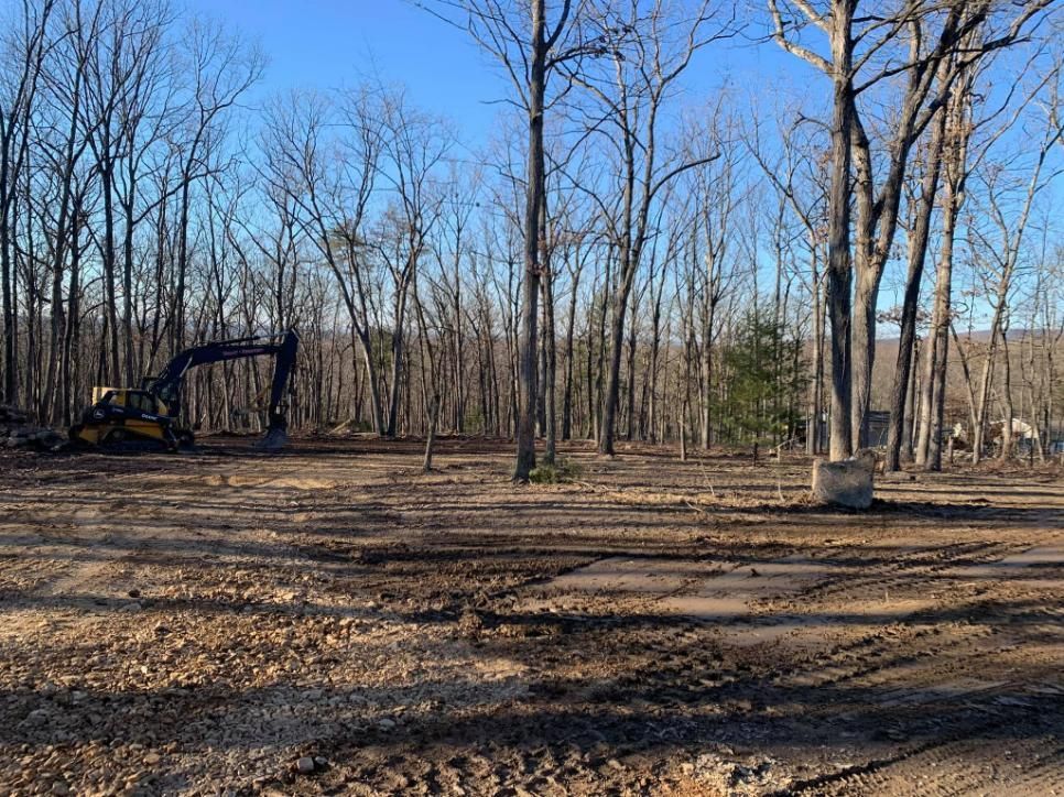 An excavator is moving dirt in a field surrounded by trees.