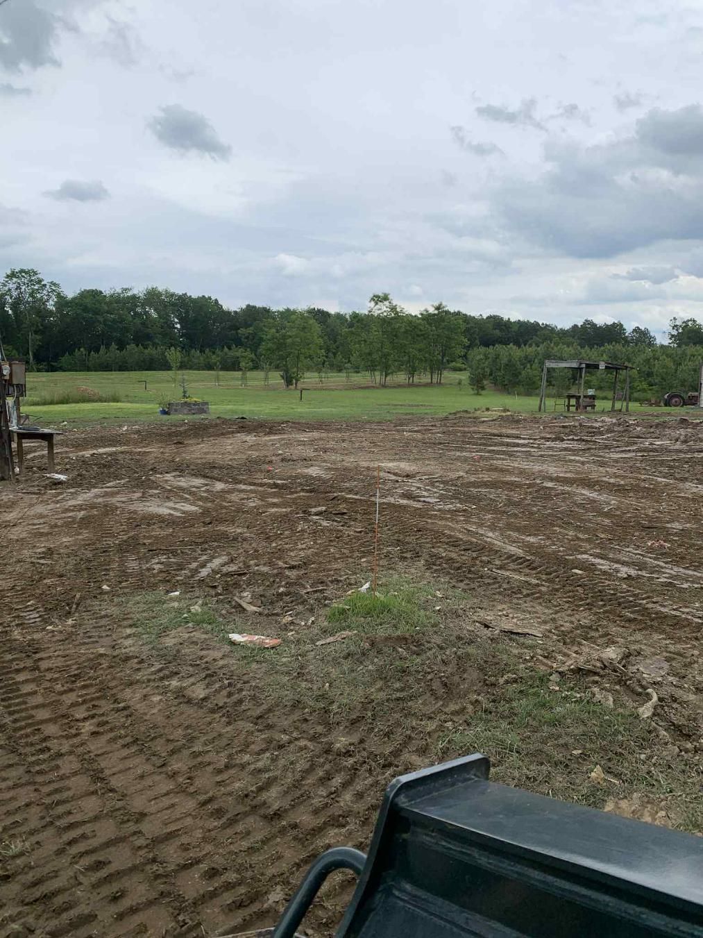 A tractor is driving through a dirt field with trees in the background.