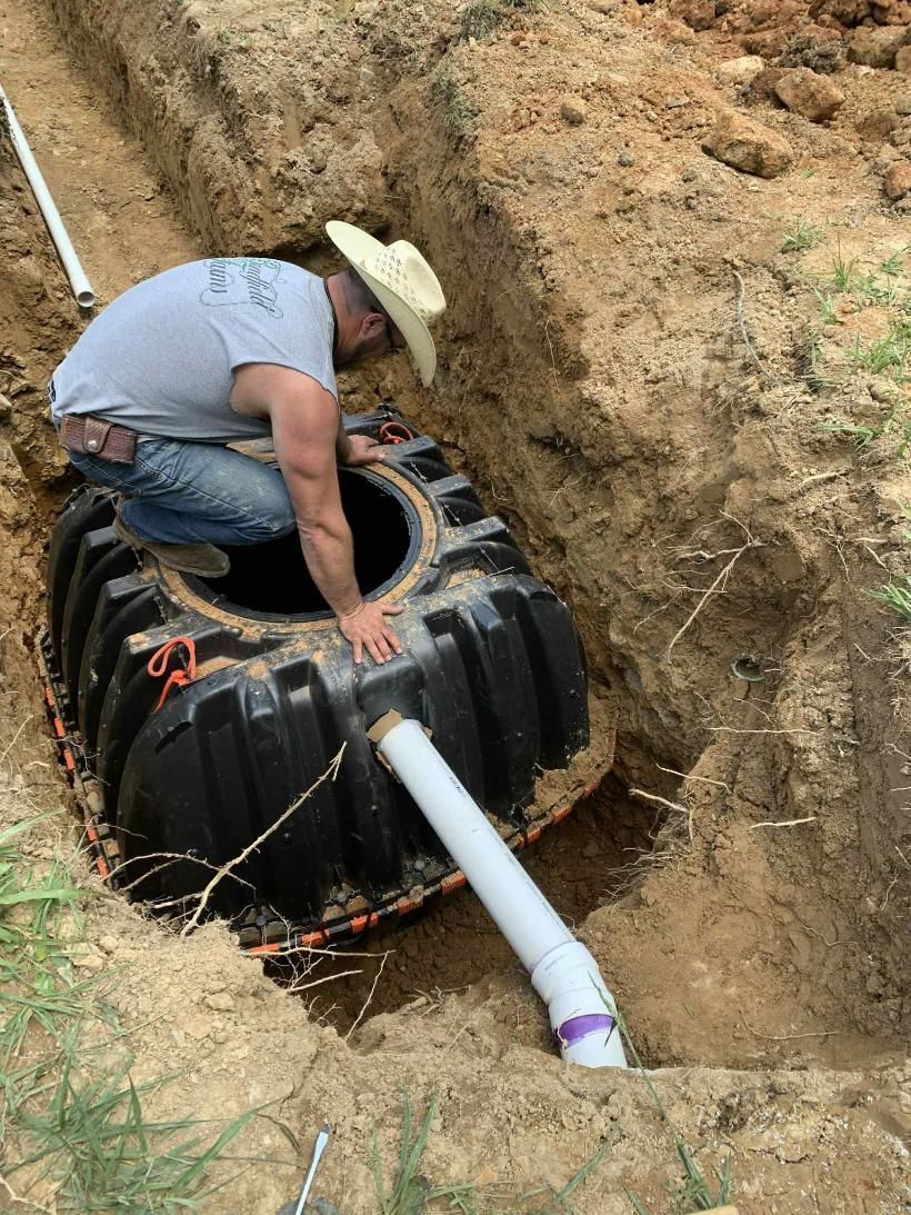 A man in a cowboy hat is working on a septic tank in the dirt.