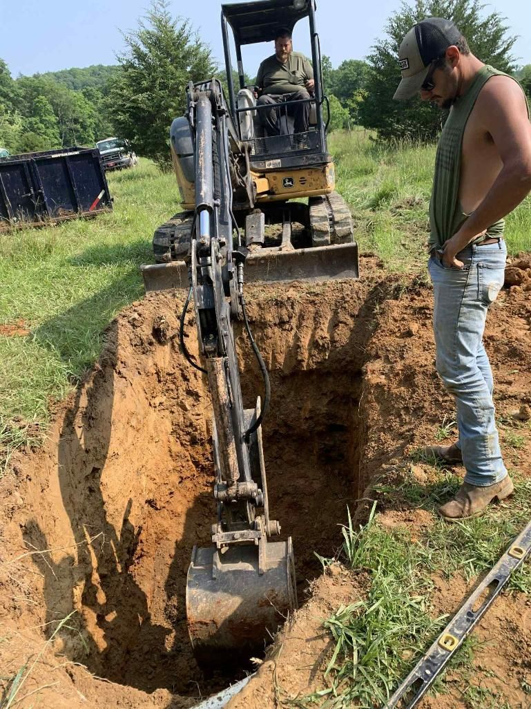 A man is standing next to a bulldozer digging a hole in the ground.