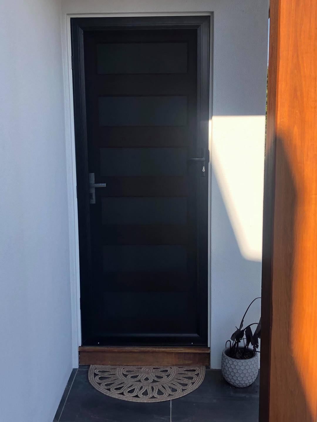 A Black Door With A Rug On The Floor In Front Of It — Central Coast Flyscreen Service In West Gosford, NSW