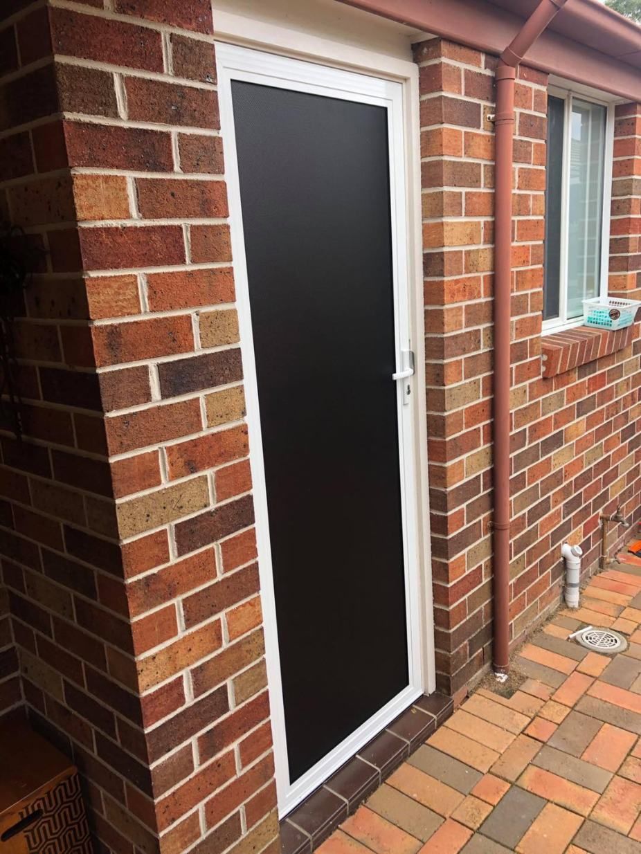 A Black Door Is On The Side Of A Brick Building — Central Coast Flyscreen Service In Woy Woy, NSW