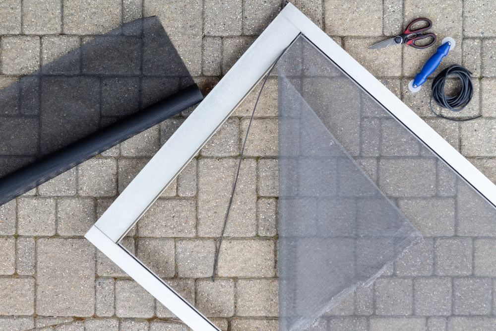 A Fly Screen Is Sitting On A Brick Floor Next To A Pair Of Scissors — Central Coast Flyscreen Service In Woongarah, NSW