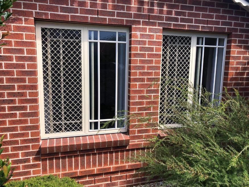 A Brick Building With Two Windows And A Bush In Front Of It — Central Coast Flyscreen Service In West Gosford, NSW