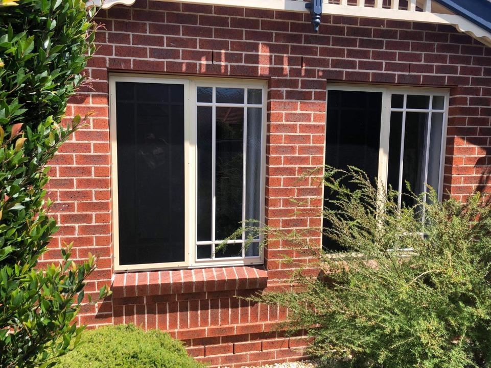 A Brick House With Two Windows And A Bush In Front Of It — Central Coast Flyscreen Service In West Gosford, NSW